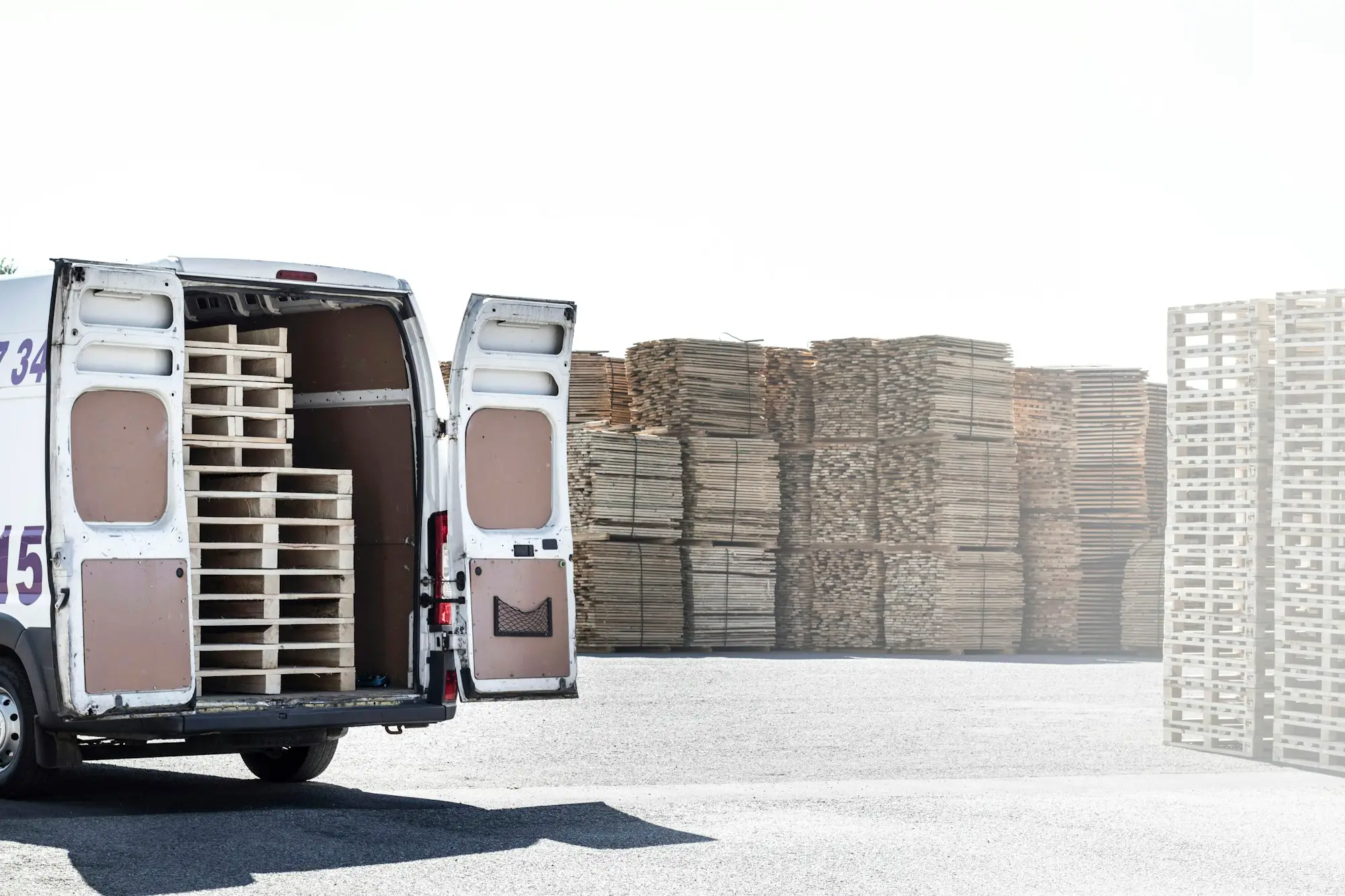 Courier van with doors open being loaded beside stacked pallets